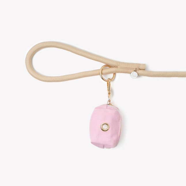 Pink pouch with gold ring on a beige strap against a white background