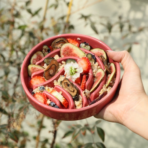 Hand holding a pink puzzle feeder filled with a colorful fruit salad against a natural background