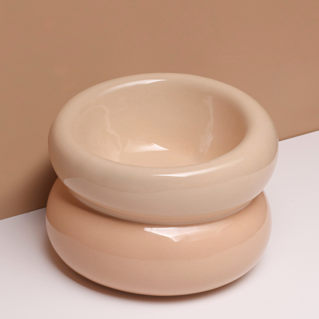 A beige ceramic bowl on a white surface with a beige background