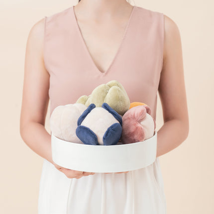 Person holding a white box with colorful plush toys against a light pink background