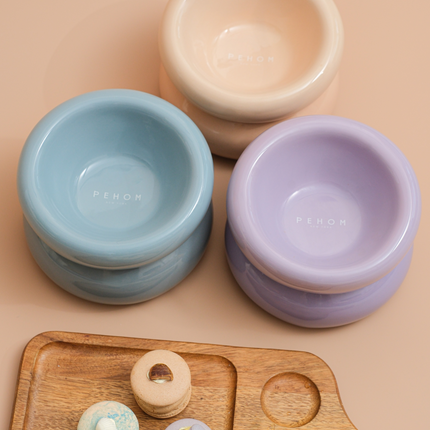 Three ceramic bowls in beige, blue, and purple on a wooden board with pastries.