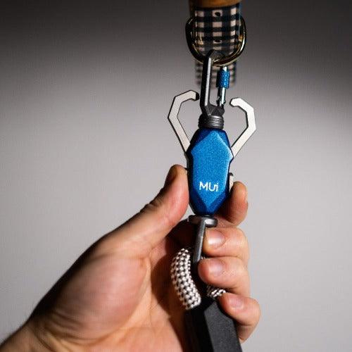 Blue multi-tool keychain held by a hand against a gray background