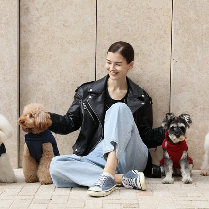 Woman sitting with four dogs wearing small jackets in front of a beige wall.