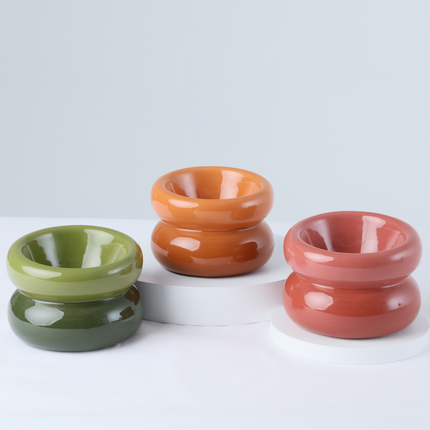 Three ceramic bowls in green, orange, and red on a white background