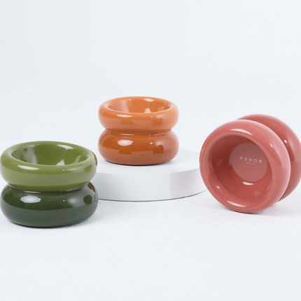 Three ceramic bowls in green, orange, and pink on a white background