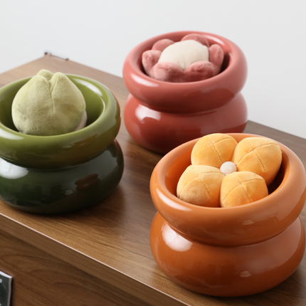 Three ceramic containers in green, red, and orange with small round items on a wooden surface.