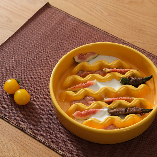 Yellow ceramic pet feeding bowl with wavy design on a brown placemat