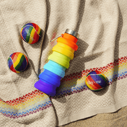 Collapsible rainbow-colored water bottle and two rainbow balls on a textured fabric background