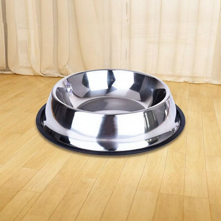 Stainless steel dog bowl on a wooden floor with beige curtains in the background