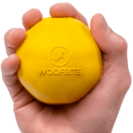 Yellow dog toy with 'WOOFBITE' branding held in a hand against a white background