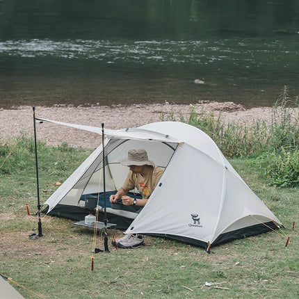 Person camping by a river with a tent and fishing gear.