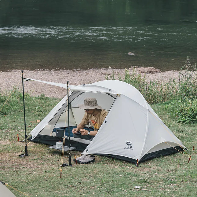 Person camping by a river with a tent and fishing gear.