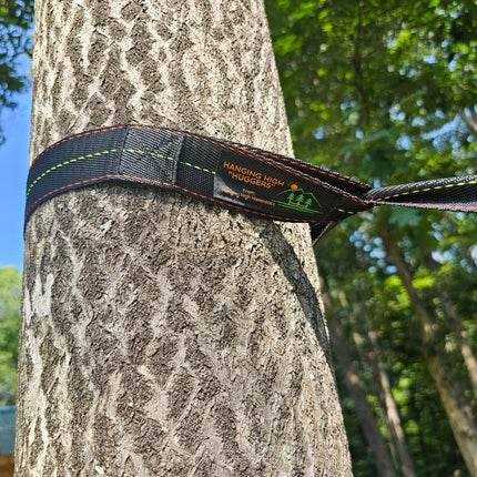 Tree strap labeled 'Hanging High Huggers' wrapped around a tree trunk with a forest background.
