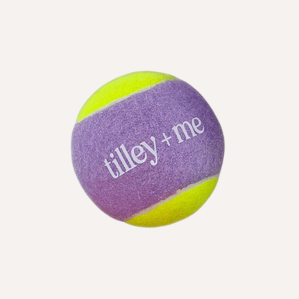 Purple and yellow tennis ball with 'tilley + me' branding on a white background