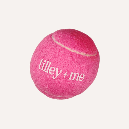 Pink tennis ball with 'tilley + me' branding on a white background