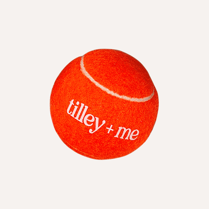 Orange tennis ball with 'tilley + me' branding on a white background